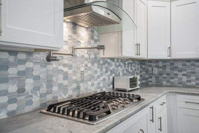 kitchen with decorative backsplash, light stone countertops, extractor fan, white cabinetry, and stainless steel gas stovetop