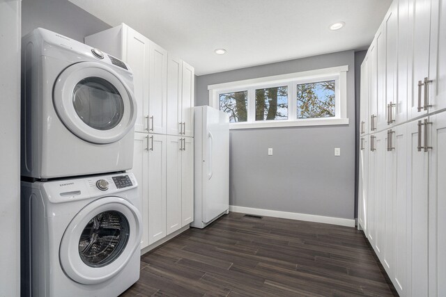 clothes washing area featuring stacked washer / dryer, dark wood-type flooring, and cabinets