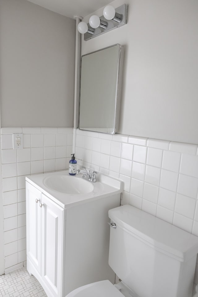 bathroom with toilet, vanity, tile patterned floors, and tile walls