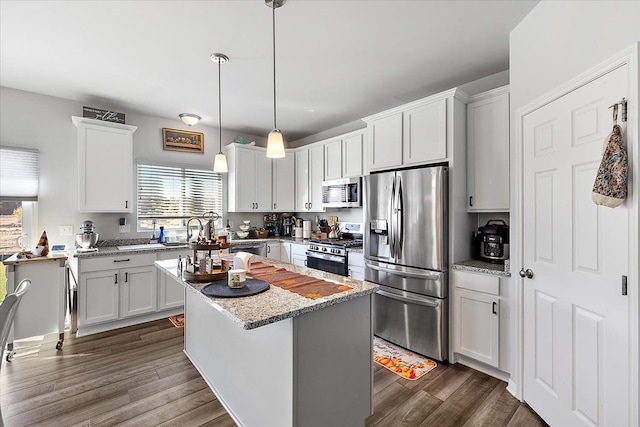 kitchen featuring pendant lighting, appliances with stainless steel finishes, a kitchen island, light stone counters, and white cabinetry