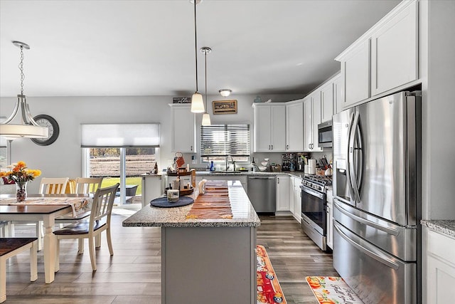 kitchen featuring pendant lighting, appliances with stainless steel finishes, a kitchen island, light stone counters, and white cabinetry