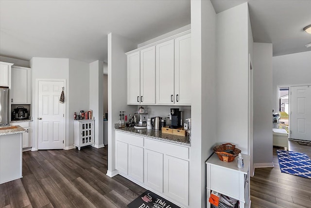 kitchen featuring stone countertops, white cabinetry, dark hardwood / wood-style floors, and stainless steel refrigerator