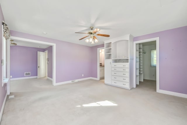 unfurnished bedroom featuring a closet, light colored carpet, a walk in closet, and ensuite bath