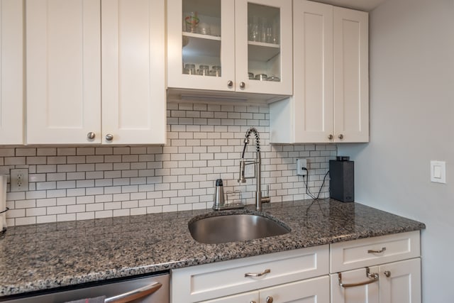 kitchen with white cabinetry, sink, stainless steel dishwasher, dark stone countertops, and decorative backsplash