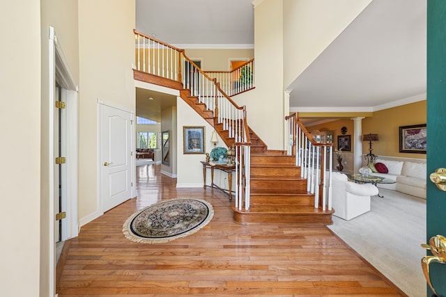 foyer featuring a towering ceiling, light hardwood / wood-style floors, decorative columns, and ornamental molding