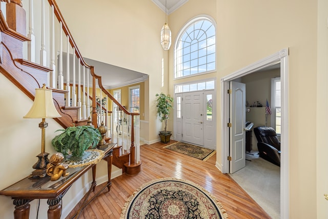 entryway with a high ceiling, light hardwood / wood-style floors, and ornamental molding