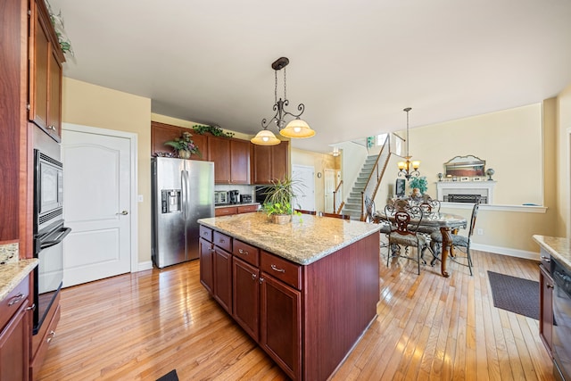 kitchen with appliances with stainless steel finishes, light wood-type flooring, decorative light fixtures, and a kitchen island