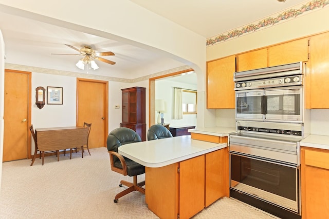 kitchen featuring a kitchen breakfast bar, kitchen peninsula, ceiling fan, and light colored carpet