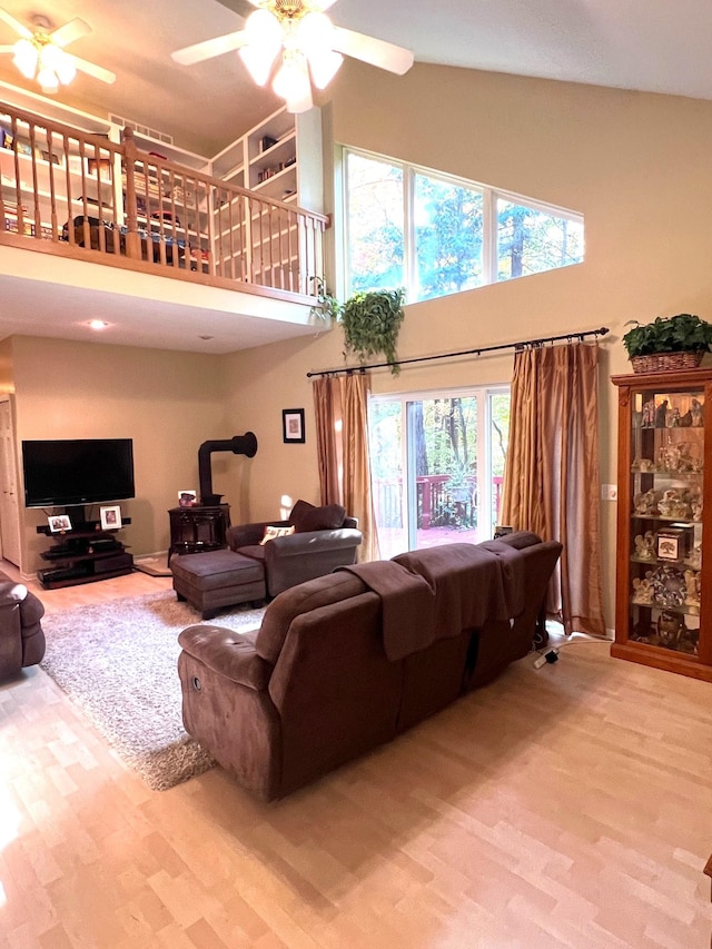 living room with wood-type flooring, a wood stove, a wealth of natural light, and ceiling fan