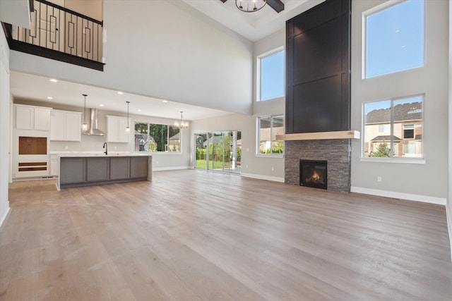 unfurnished living room with a stone fireplace, light hardwood / wood-style floors, a towering ceiling, ceiling fan with notable chandelier, and sink