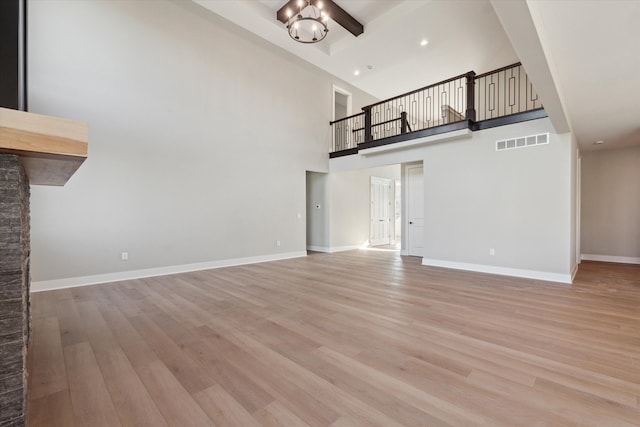 unfurnished living room with a high ceiling, light wood-type flooring, and a chandelier