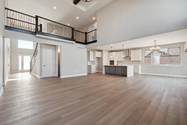 unfurnished living room with a towering ceiling, a chandelier, and hardwood / wood-style floors