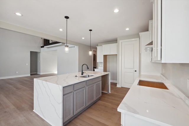 kitchen with sink, white cabinets, hanging light fixtures, light stone countertops, and a center island with sink