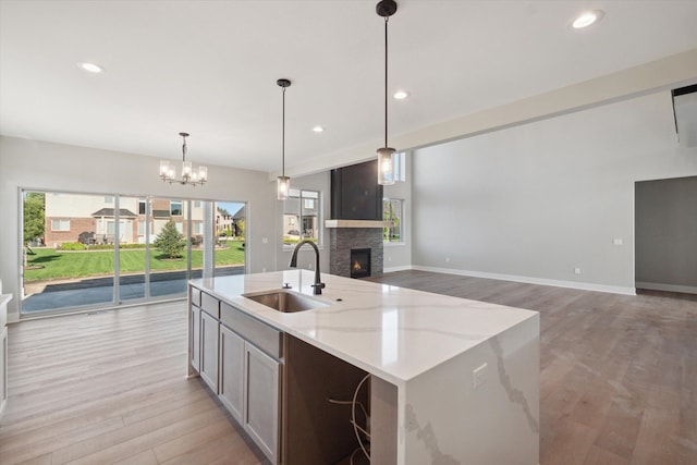 kitchen featuring light stone counters, pendant lighting, an island with sink, light wood-type flooring, and sink