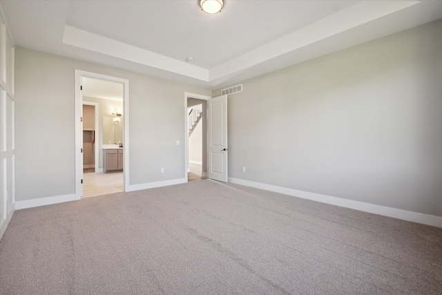 unfurnished bedroom featuring ensuite bath, light carpet, and a tray ceiling