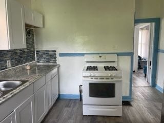 kitchen featuring dark hardwood / wood-style floors, light stone counters, white cabinetry, and gas range gas stove