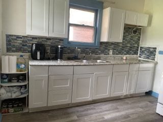 kitchen with light wood-type flooring, tasteful backsplash, light stone counters, sink, and white cabinets