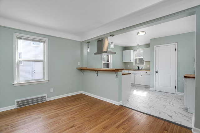 kitchen with pendant lighting, a breakfast bar, white cabinets, wall chimney range hood, and kitchen peninsula