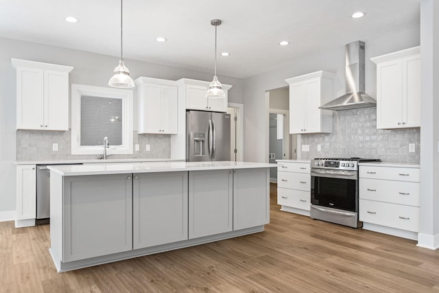 kitchen featuring white cabinets, wall chimney exhaust hood, stainless steel appliances, and a kitchen island