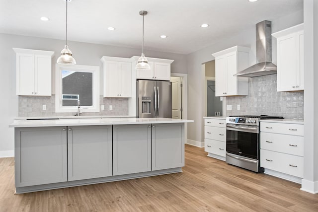 kitchen featuring wall chimney exhaust hood, stainless steel appliances, light hardwood / wood-style floors, decorative light fixtures, and a kitchen island