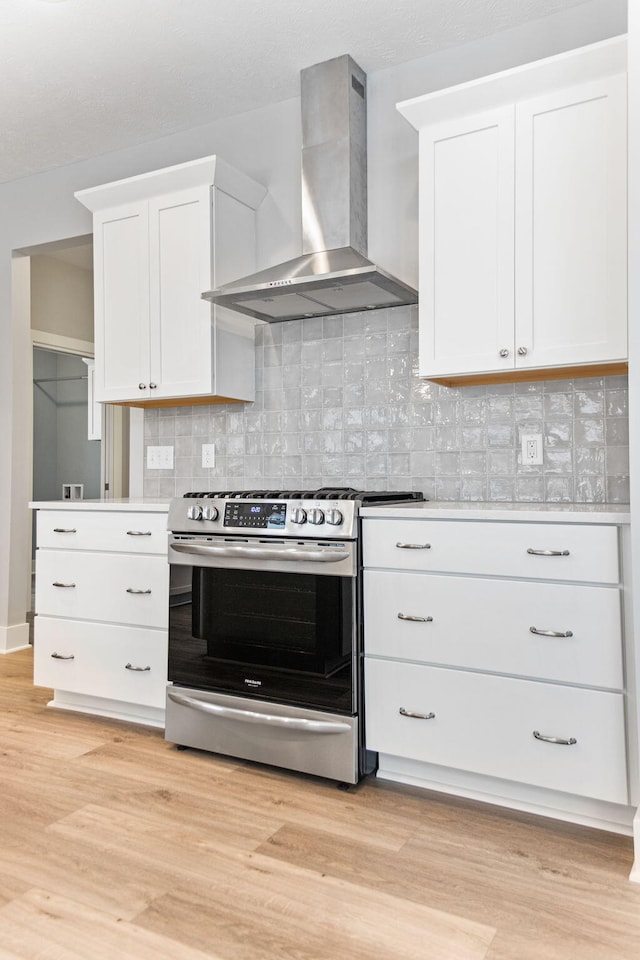 kitchen with decorative backsplash, stainless steel range oven, light hardwood / wood-style flooring, and wall chimney range hood