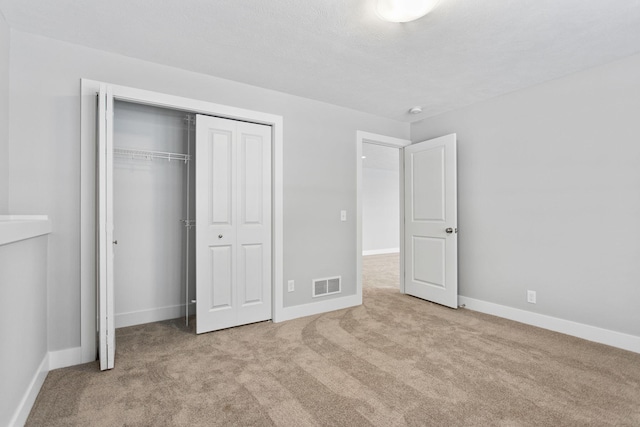 unfurnished bedroom with a textured ceiling, light carpet, and a closet