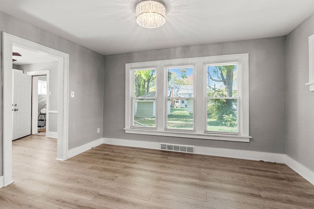 empty room with light hardwood / wood-style floors and an inviting chandelier