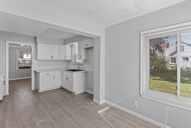 kitchen featuring sink, light wood-type flooring, white cabinetry, and backsplash