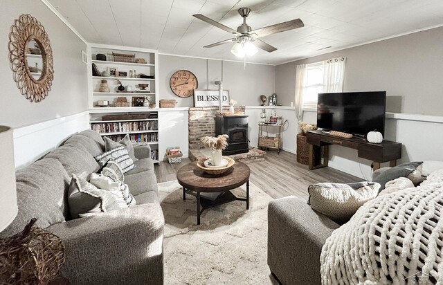 living room with a wood stove, ceiling fan, light hardwood / wood-style flooring, and ornamental molding