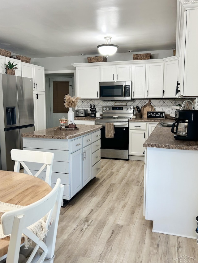 kitchen featuring decorative backsplash, appliances with stainless steel finishes, white cabinets, light hardwood / wood-style floors, and a kitchen island