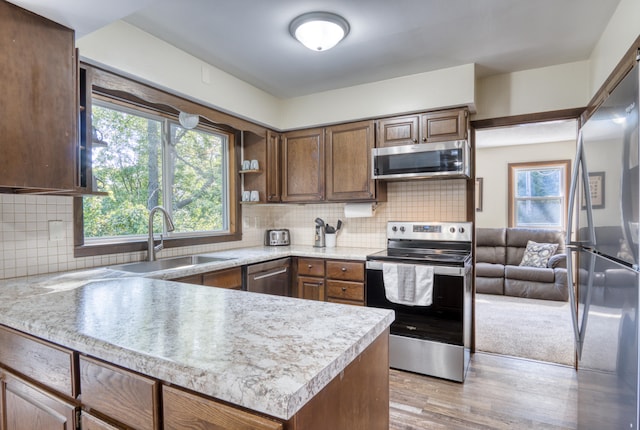 kitchen featuring kitchen peninsula, appliances with stainless steel finishes, backsplash, sink, and light hardwood / wood-style floors