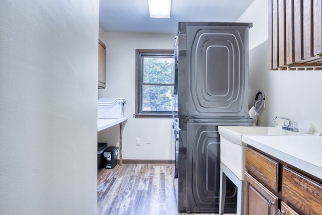 laundry room featuring cabinets, stacked washer and clothes dryer, and light hardwood / wood-style floors