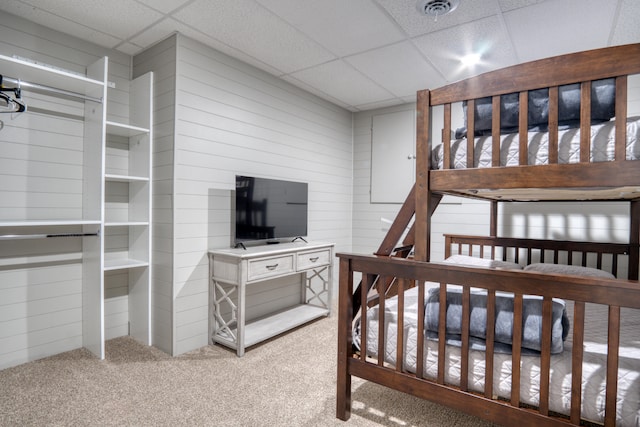 bedroom featuring carpet, a paneled ceiling, and wood walls