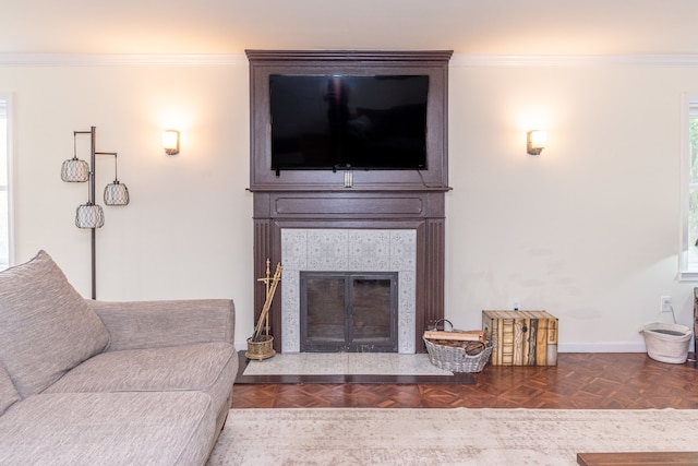 living room featuring a tiled fireplace, baseboards, and crown molding