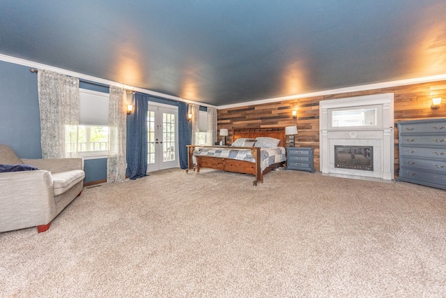 carpeted bedroom featuring wooden walls, ornamental molding, a glass covered fireplace, and french doors