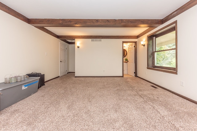 empty room with beam ceiling, visible vents, light carpet, and baseboards