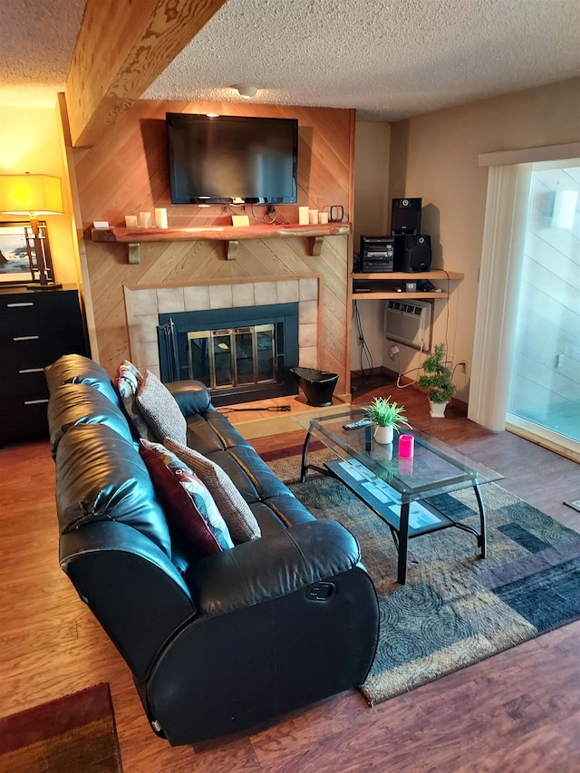 living room with wood walls, wood-type flooring, a textured ceiling, and a tile fireplace