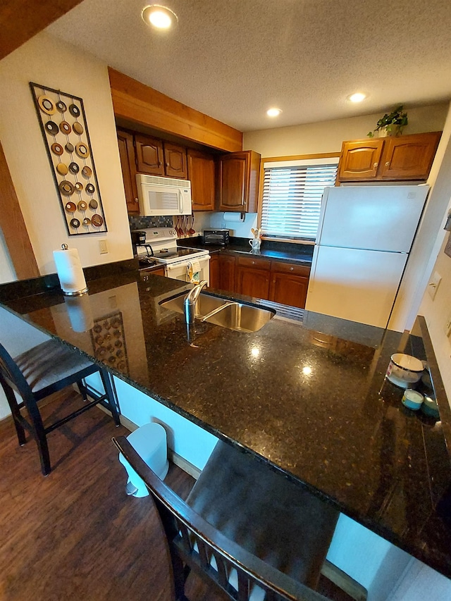 kitchen featuring white appliances, dark wood-type flooring, a textured ceiling, a kitchen bar, and kitchen peninsula