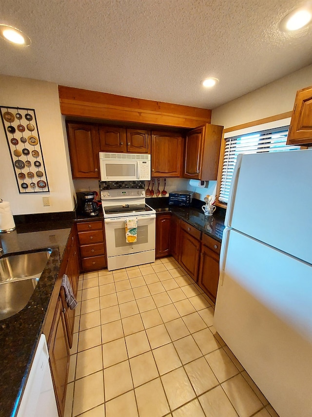 kitchen featuring a textured ceiling, white appliances, sink, light tile patterned floors, and dark stone countertops