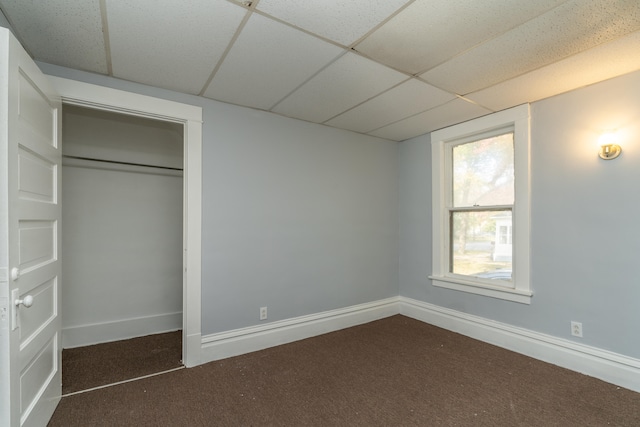 unfurnished bedroom featuring a paneled ceiling, dark carpet, and a closet