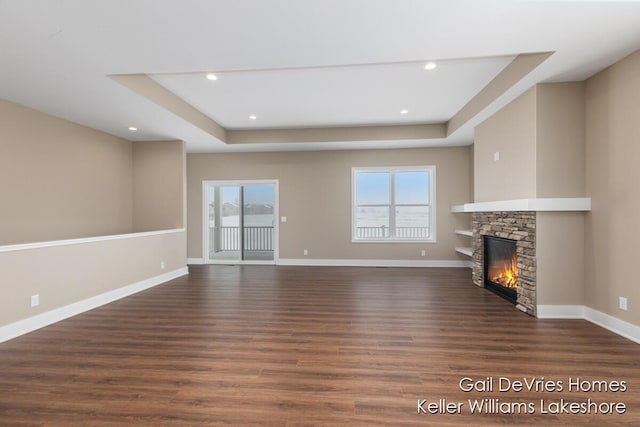 unfurnished living room featuring a wealth of natural light, dark wood finished floors, a fireplace, and baseboards