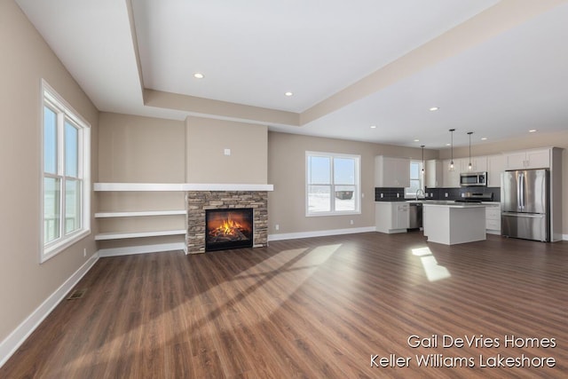 unfurnished living room featuring a stone fireplace, recessed lighting, dark wood-style flooring, visible vents, and baseboards