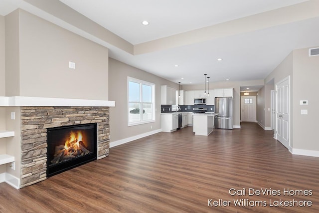 unfurnished living room with a sink, dark wood finished floors, a stone fireplace, and baseboards