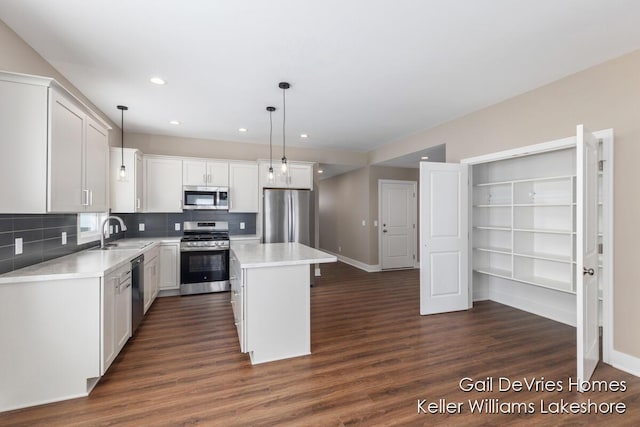 kitchen featuring stainless steel appliances, a sink, a kitchen island, light countertops, and pendant lighting