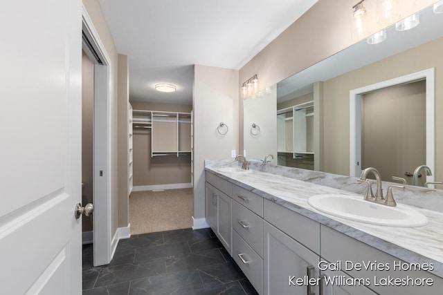 full bathroom featuring a walk in closet, a sink, baseboards, and double vanity