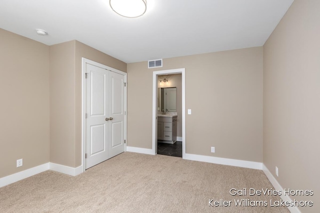 unfurnished bedroom featuring light carpet, baseboards, visible vents, ensuite bath, and a closet