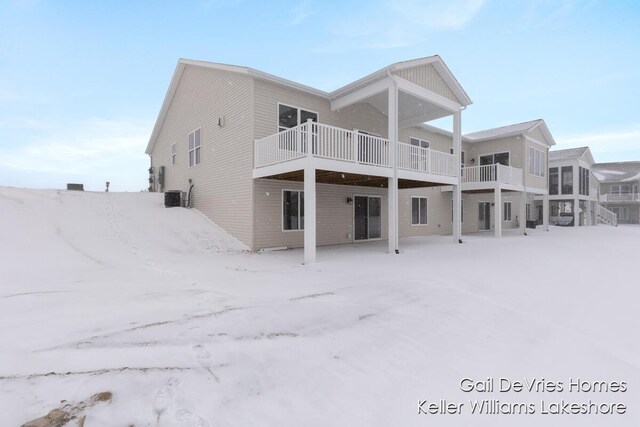 snow covered back of property with a balcony and central AC