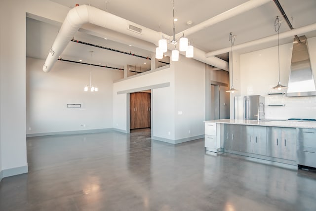 kitchen with sink, hanging light fixtures, a high ceiling, cooktop, and stainless steel fridge