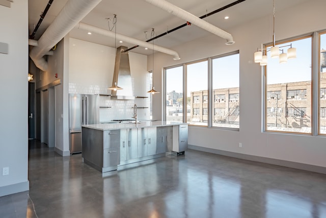 kitchen featuring a kitchen island with sink, high end refrigerator, range hood, pendant lighting, and decorative backsplash