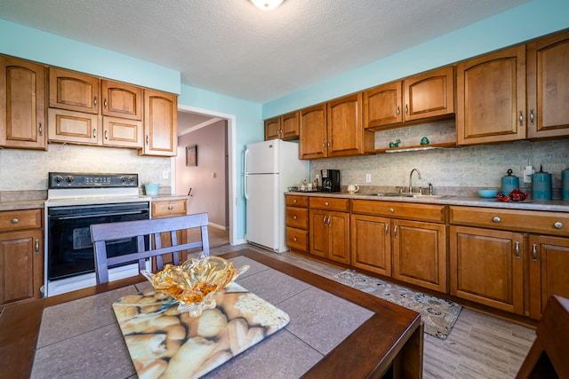 kitchen with decorative backsplash, light wood-type flooring, a textured ceiling, white appliances, and sink